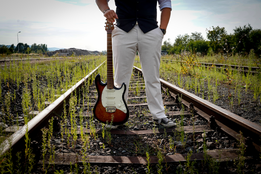 David Schneider stehend am Bahnhof, Fokus auf Gitarre.